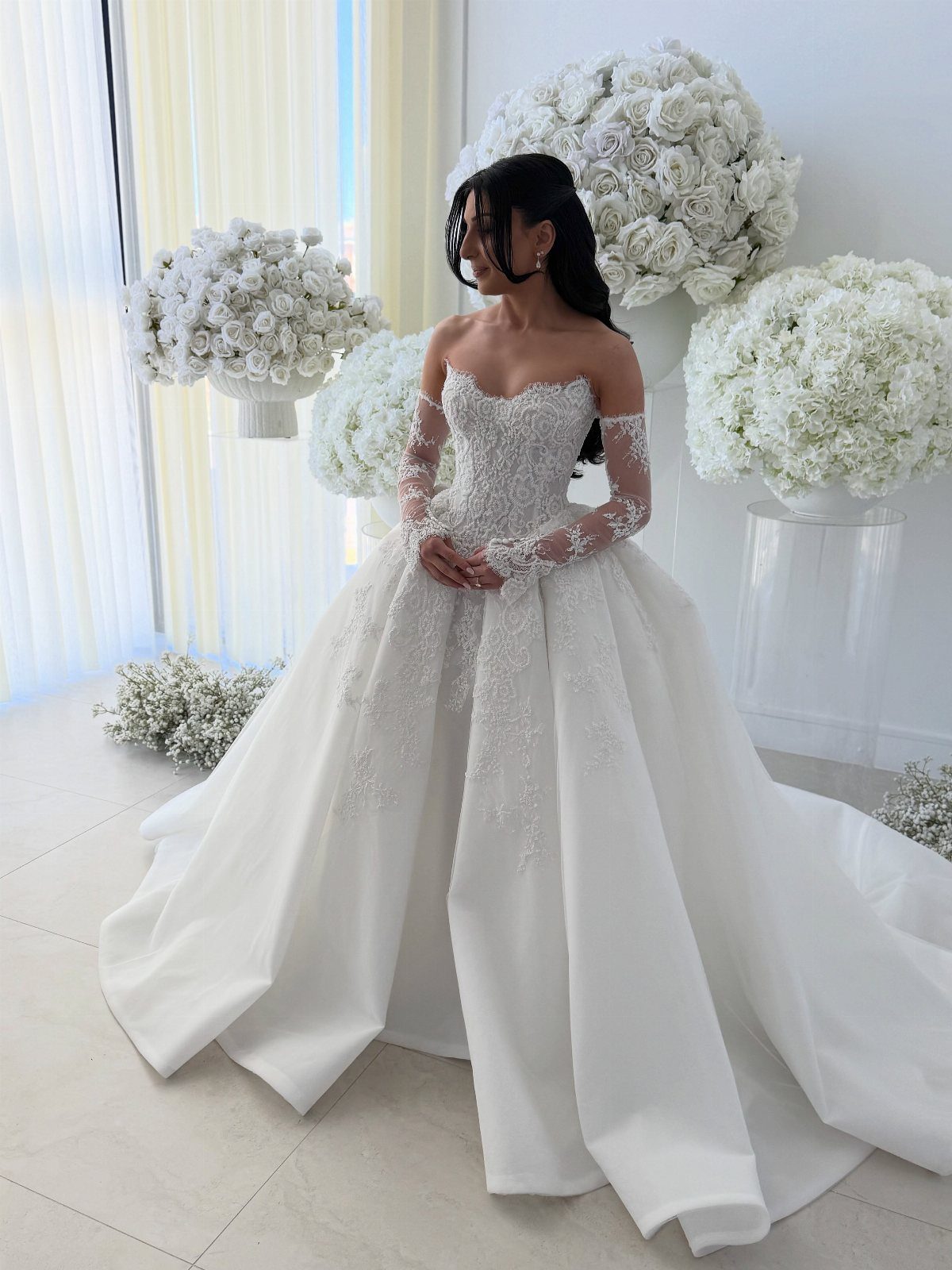 Woman in a voluminous white wedding gown with lace details and white roses.