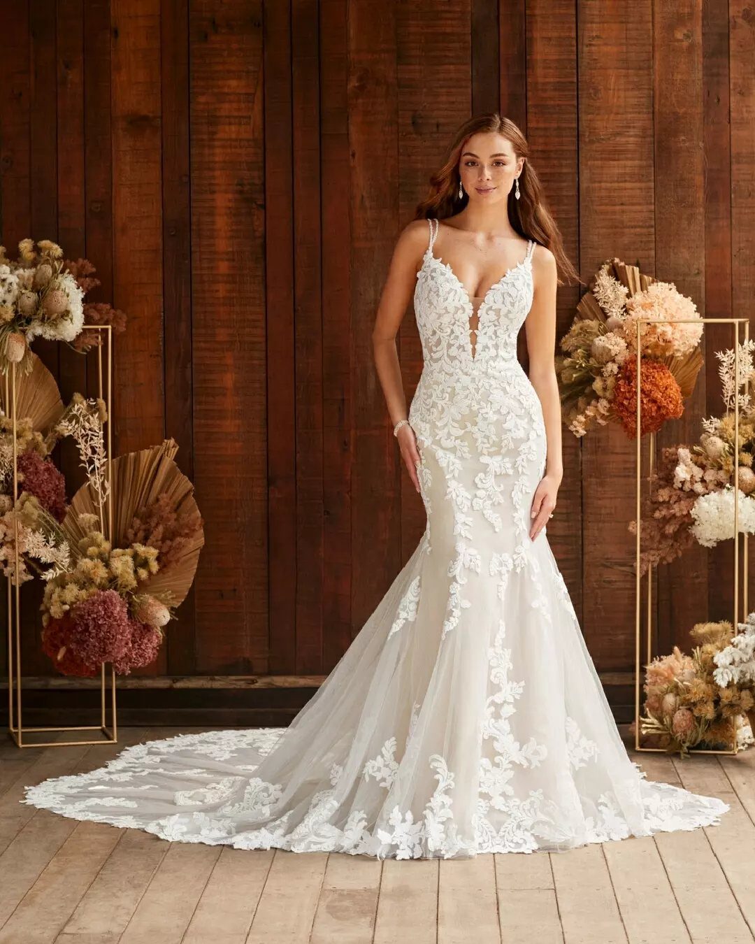 Woman in a white lace mermaid wedding dress posing against a wooden wall.