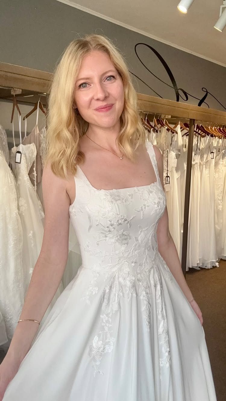Blonde woman wearing a white A-line wedding dress with a square neckline.