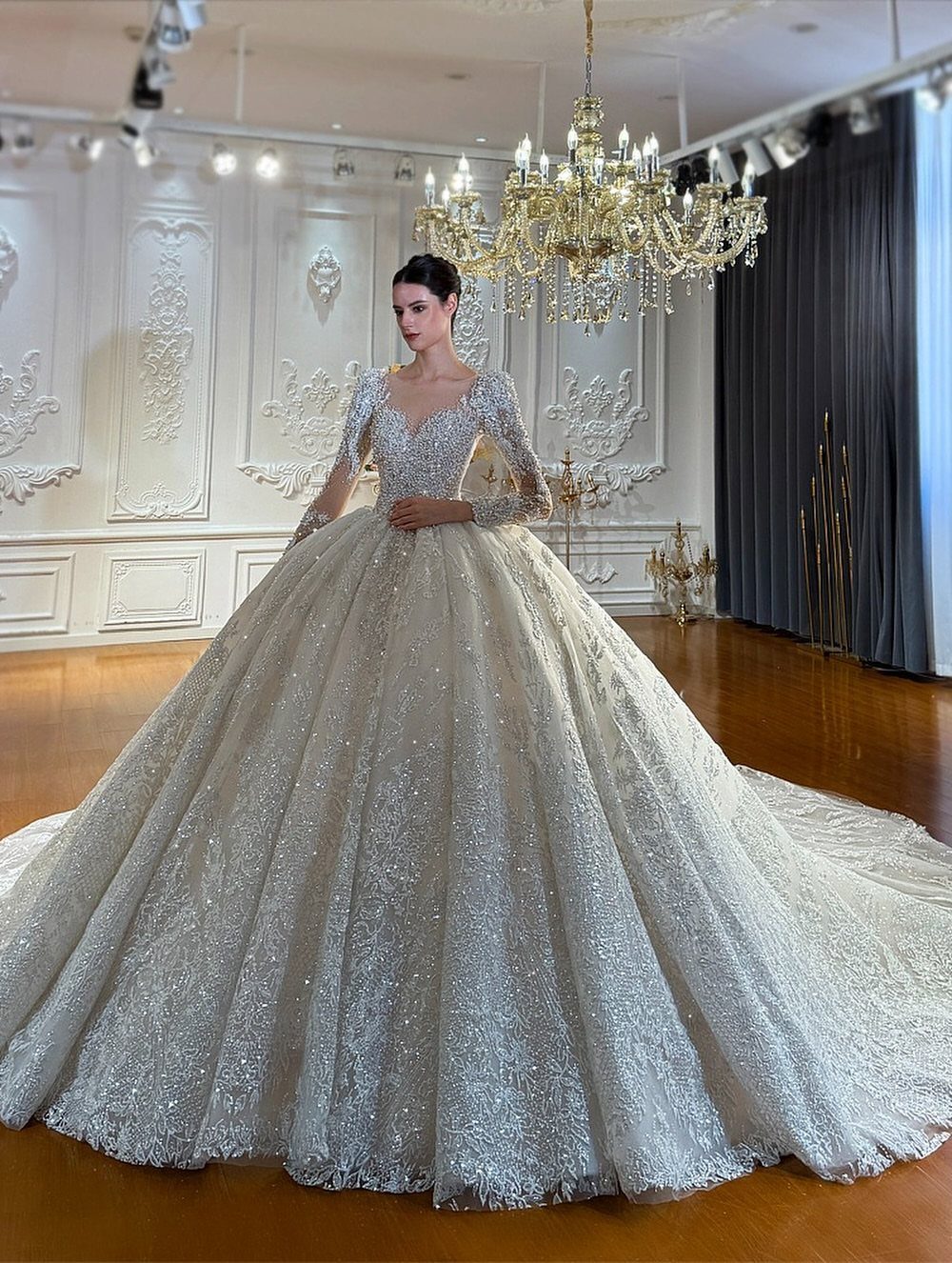 Woman in a sparkling white ballgown wedding dress standing under a crystal chandelier.