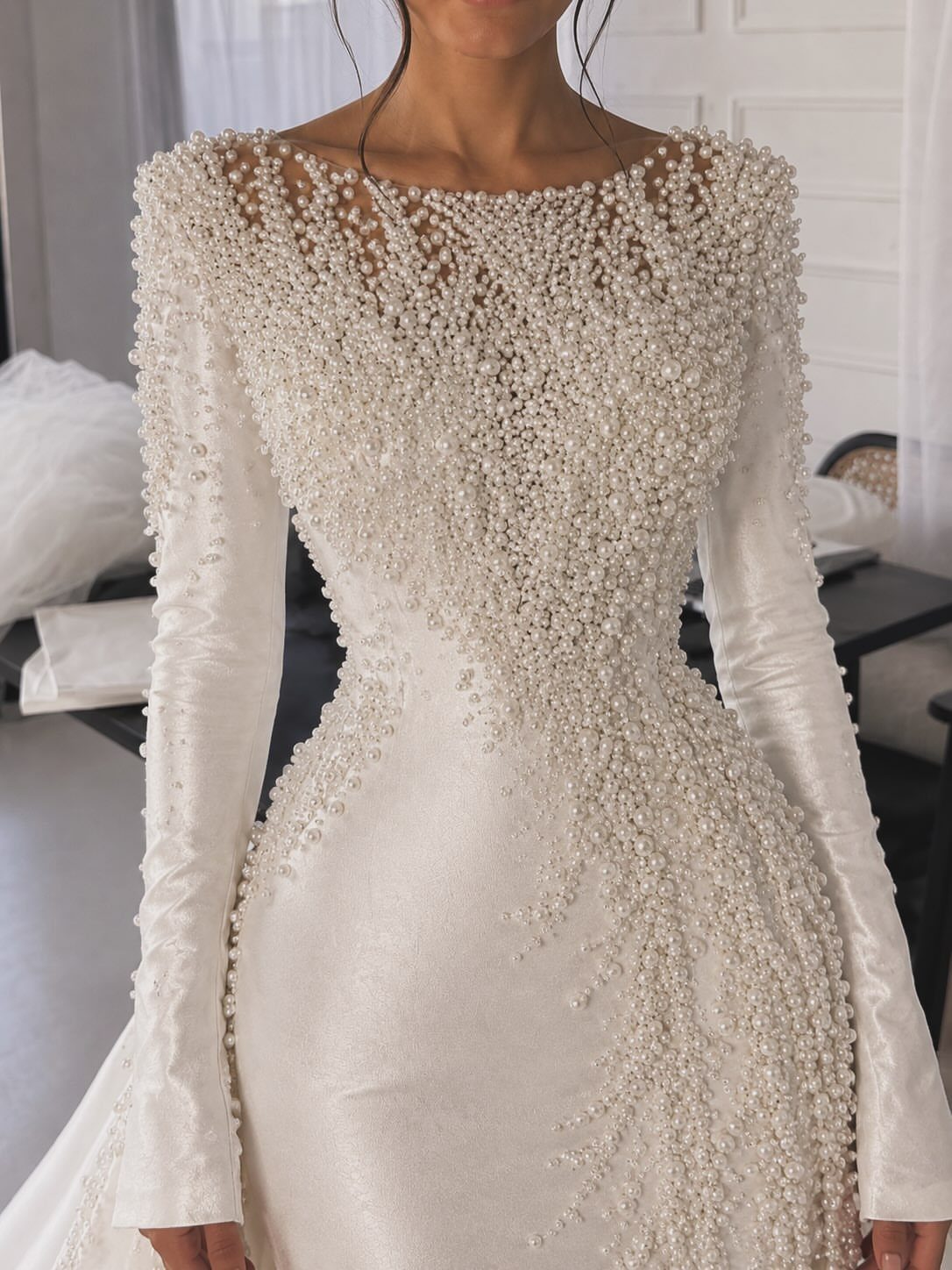 White long-sleeved wedding dress with detailed pearl beading on the bodice and skirt.