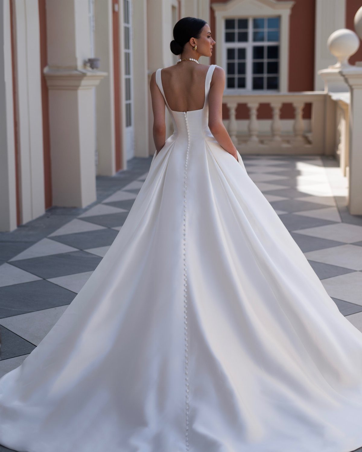Woman in a white satin wedding gown with a long train on a patio