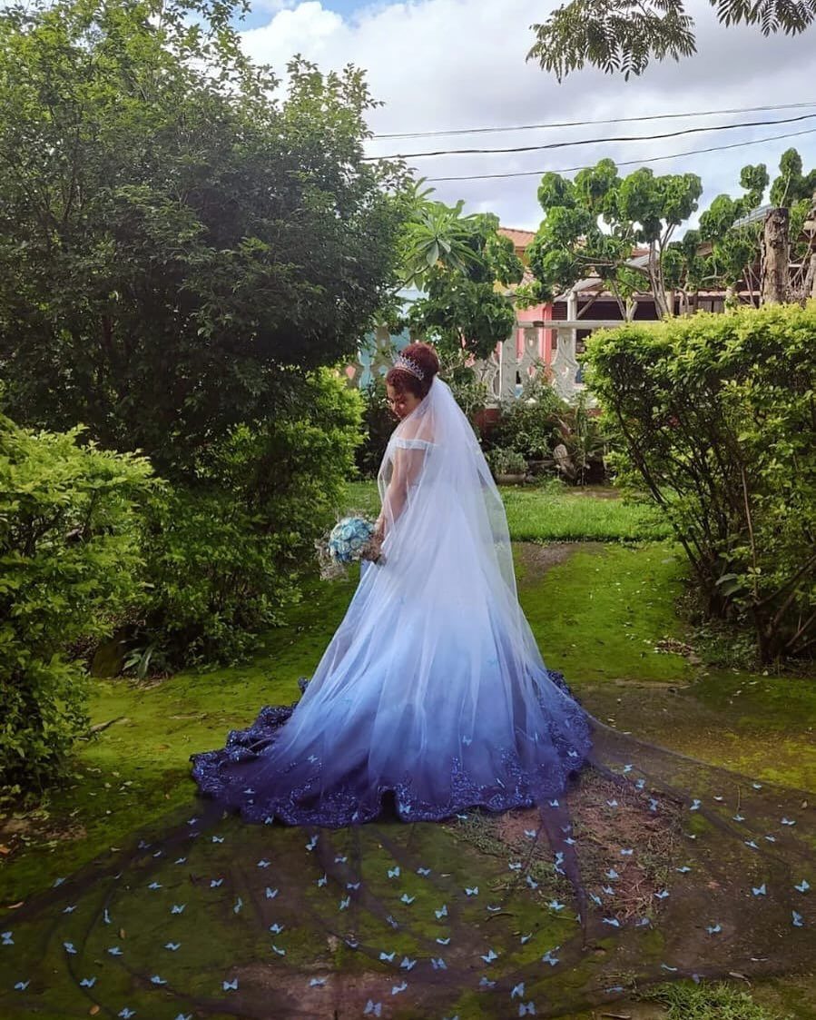 Woman in a white and blue gradient wedding dress standing in a green garden