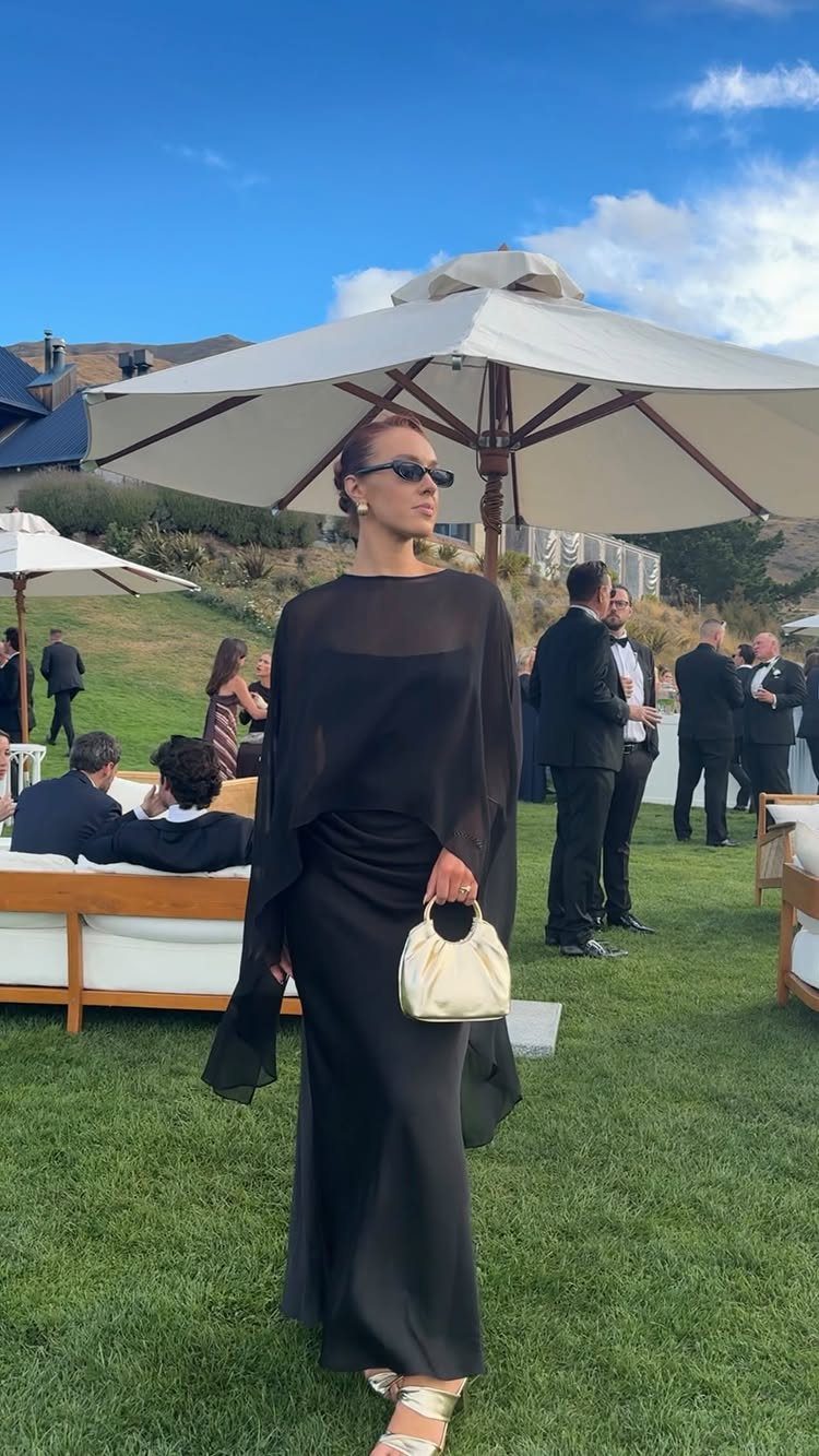 Woman in elegant long black dress and white handbag at outdoor wedding event