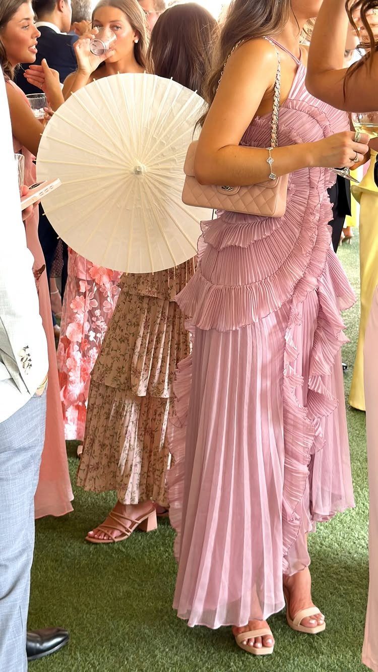 Women in elegant mauve and patterned dresses attending an outdoor wedding event.