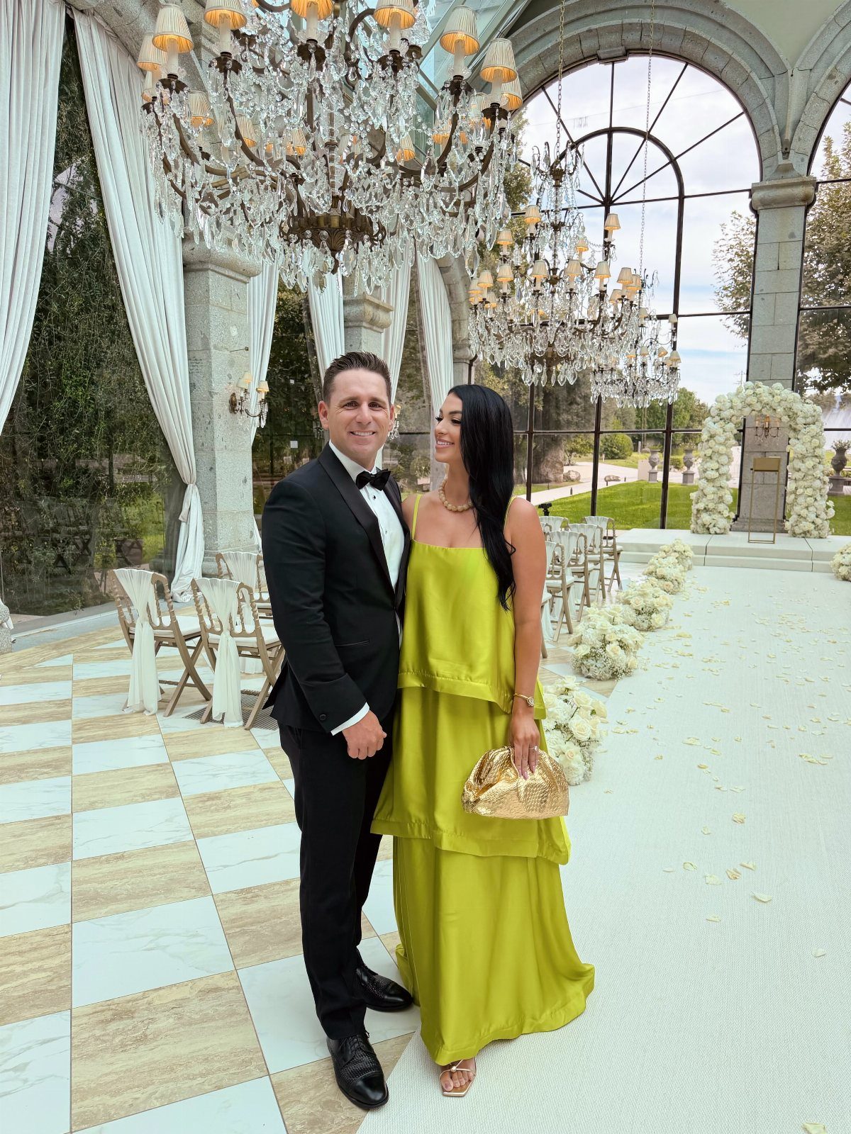 Couple in formal attire posing under crystal chandeliers in an elegant wedding venue.