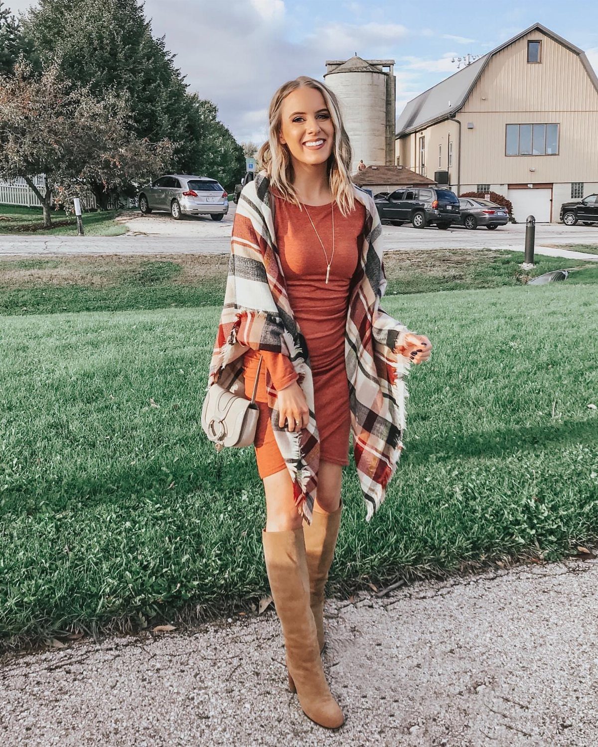Woman in rust dress and plaid shawl posing outdoors near a barn