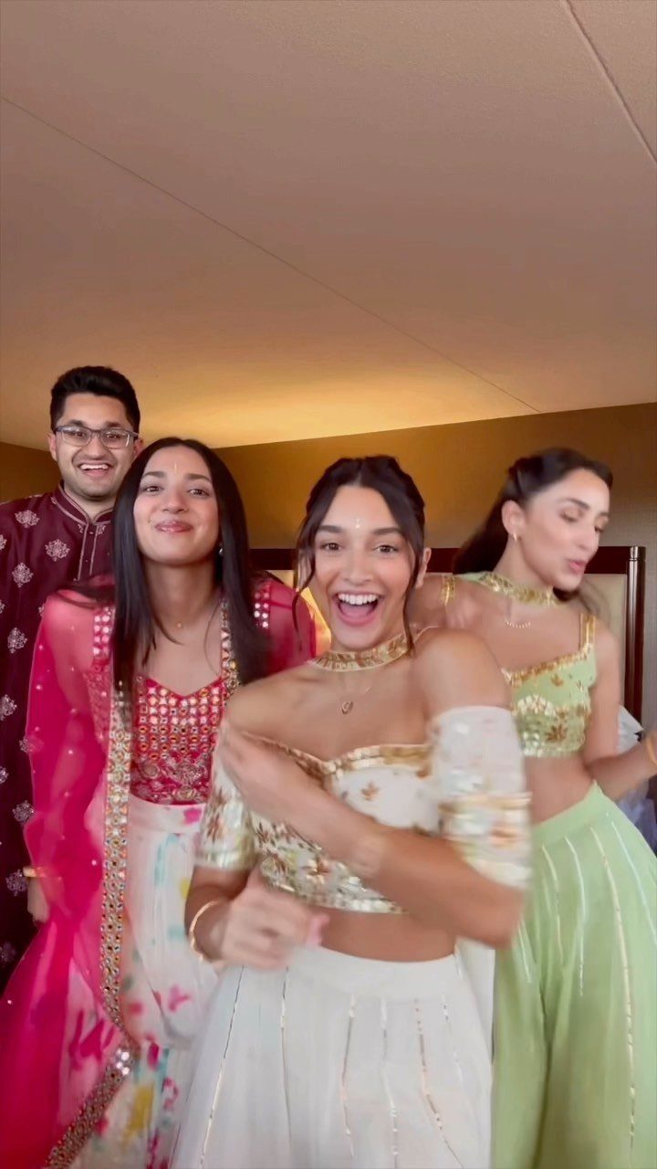 Four people wearing colorful traditional Indian wedding attire posing and smiling indoors.