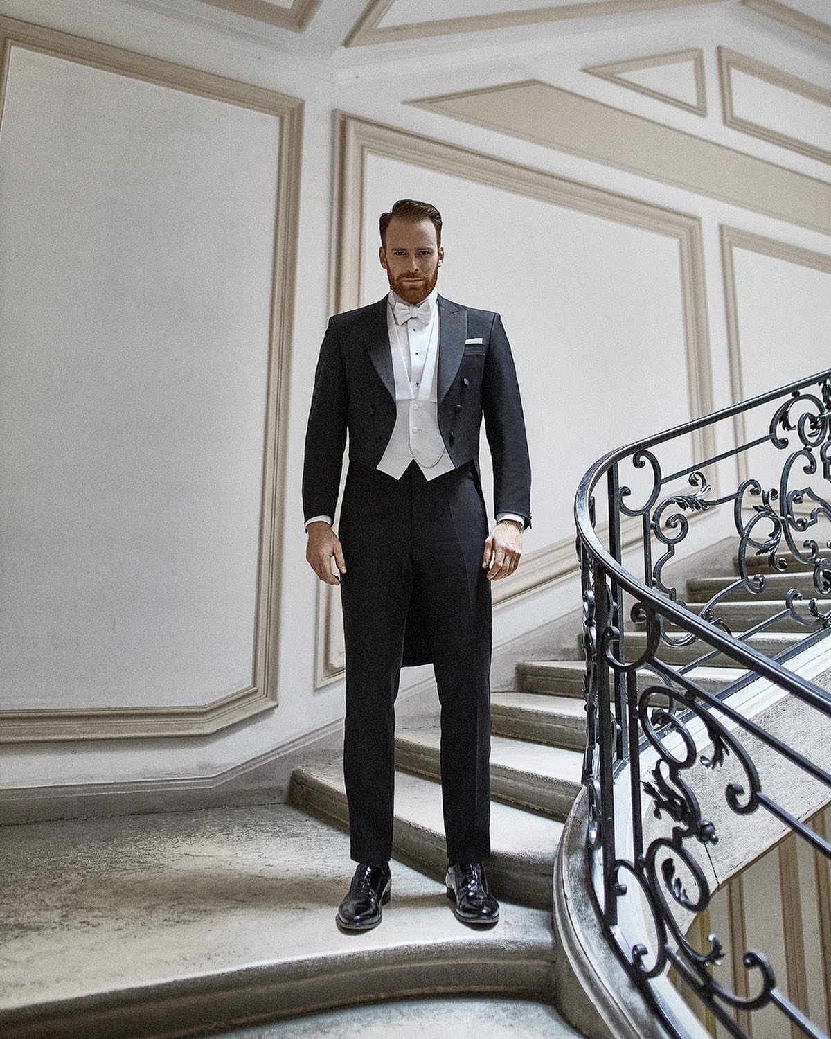 Man in a black tailcoat and white bow tie standing on a staircase