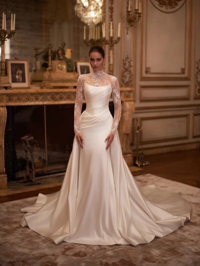 Woman in a white satin wedding dress and long-sleeved lace bolero jacket.