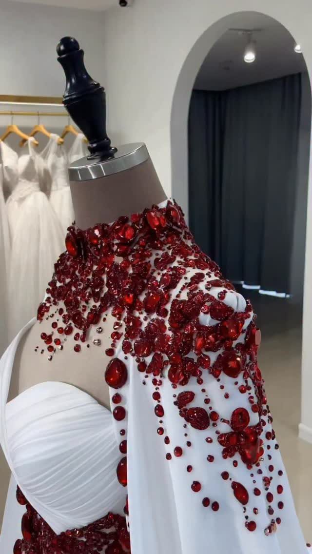 White bridal gown and bolero cape embellished with large red crystals on mannequin