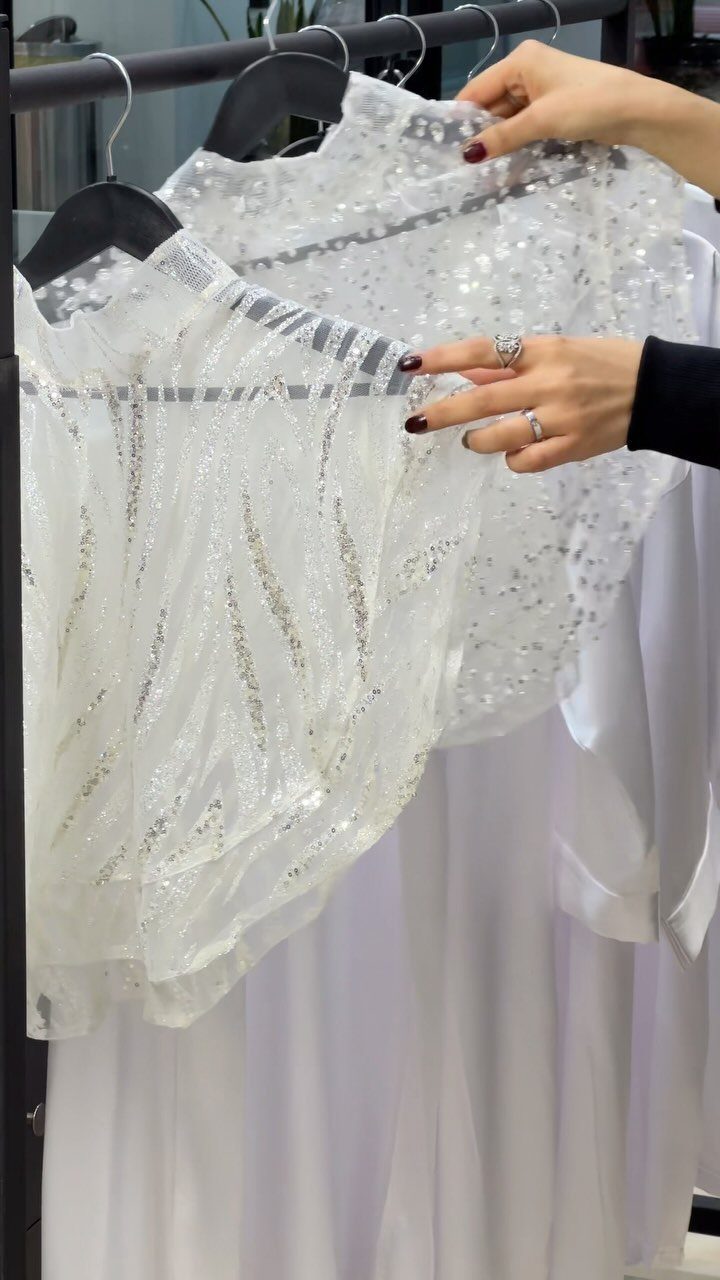 White beaded bolero jacket held up in front of a white wedding gown.