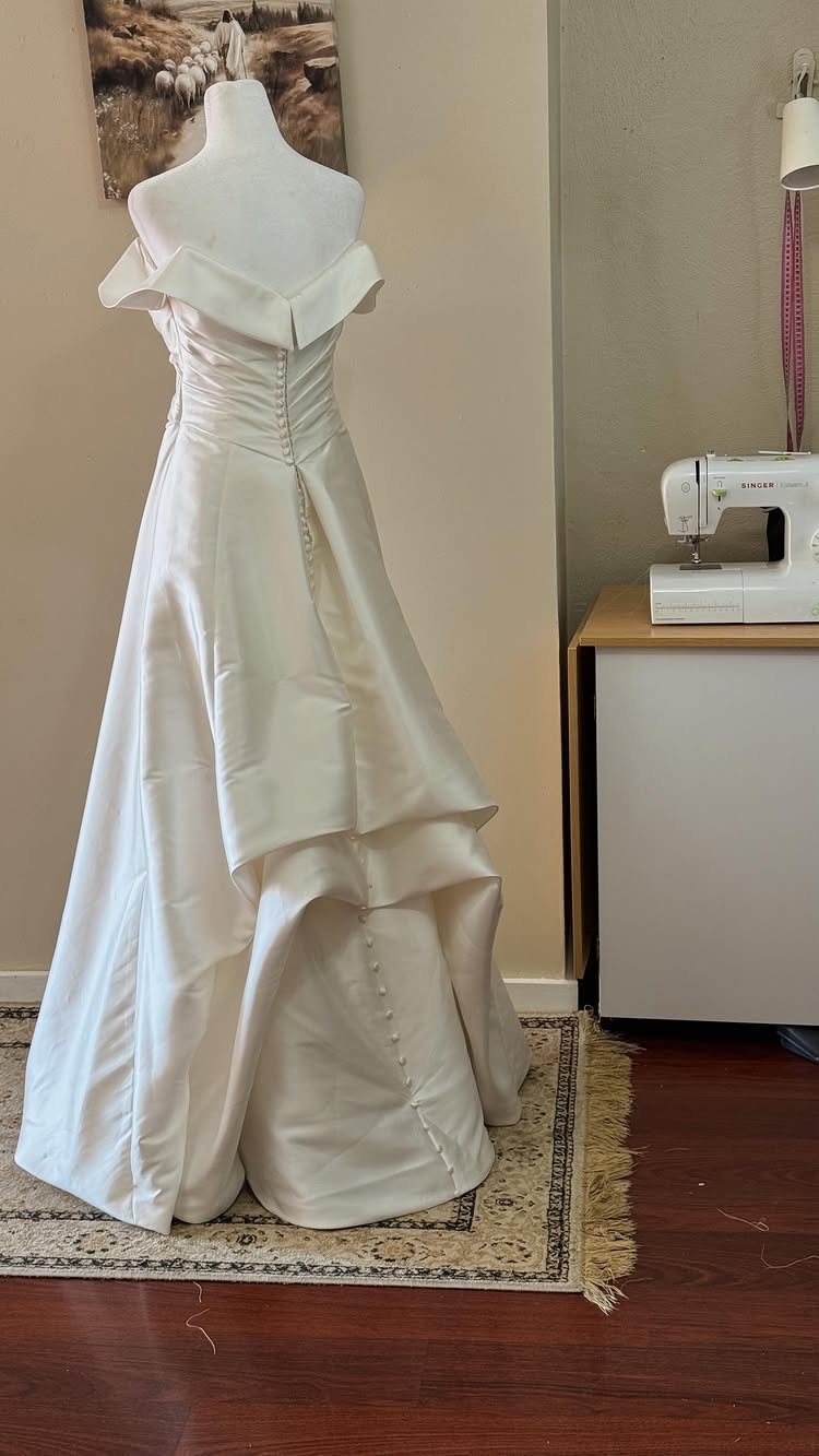 White satin wedding dress on a mannequin showing a gathered bustle at the back