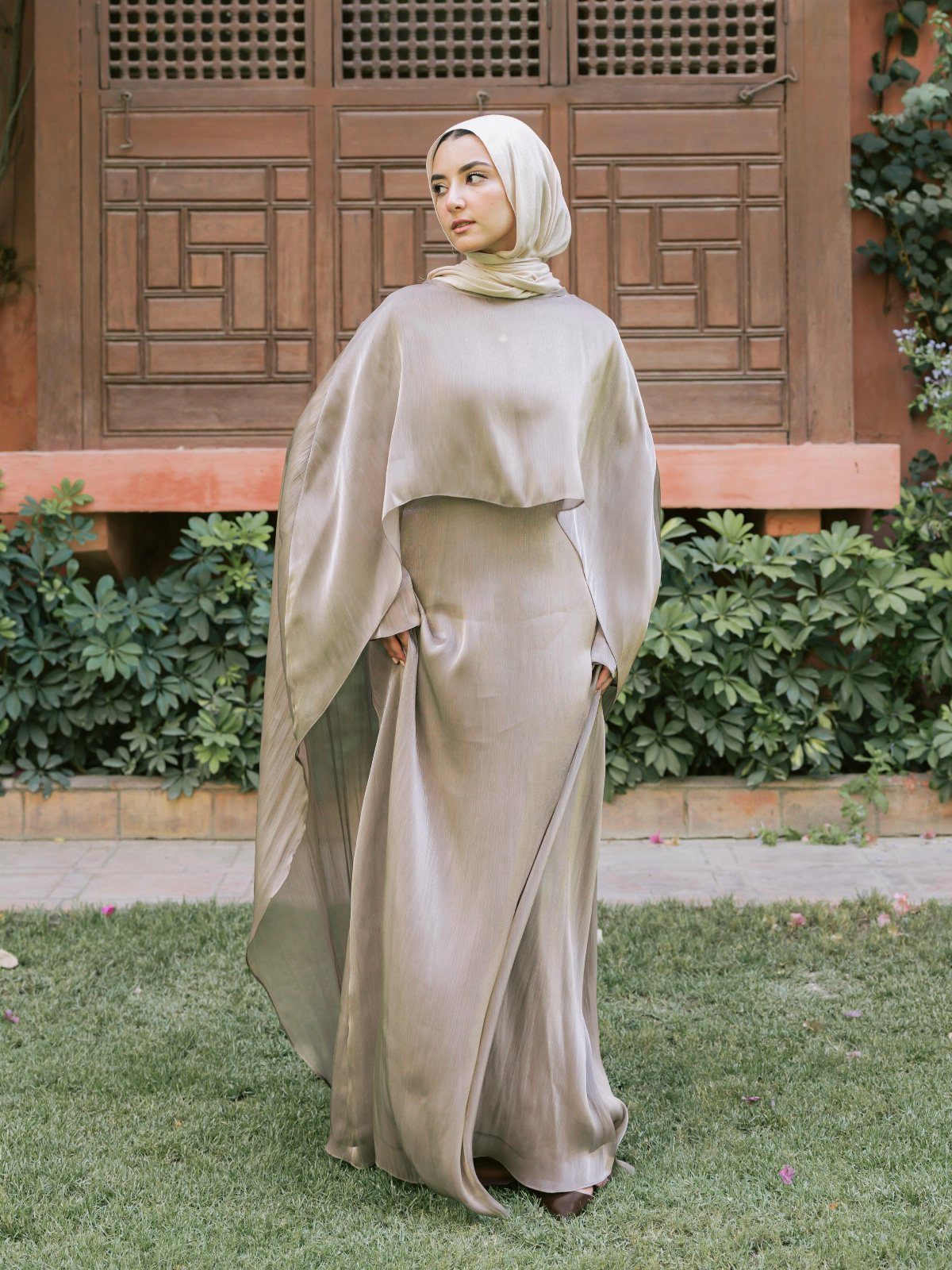 Woman in a champagne chiffon wedding gown and hijab standing on green grass