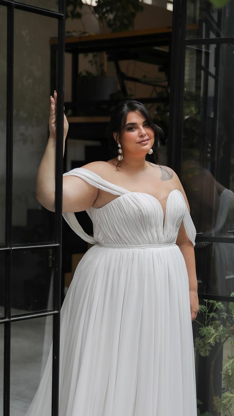 Woman in a white A-line chiffon wedding dress posing by a glass door