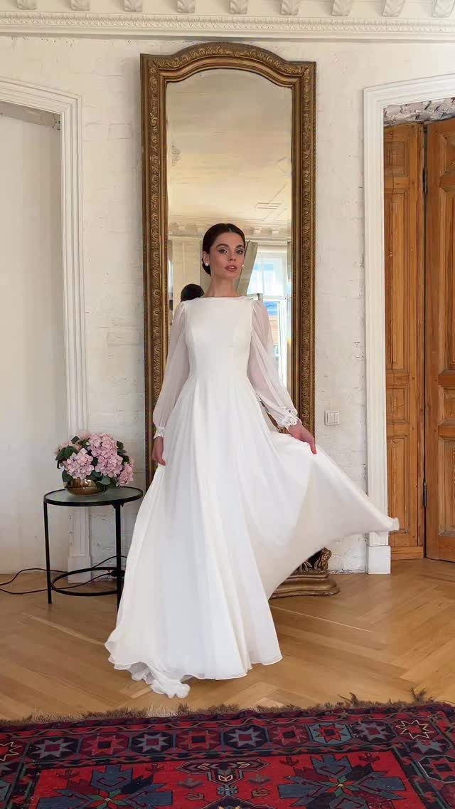 Woman in a long sleeve white chiffon wedding dress standing before a mirror