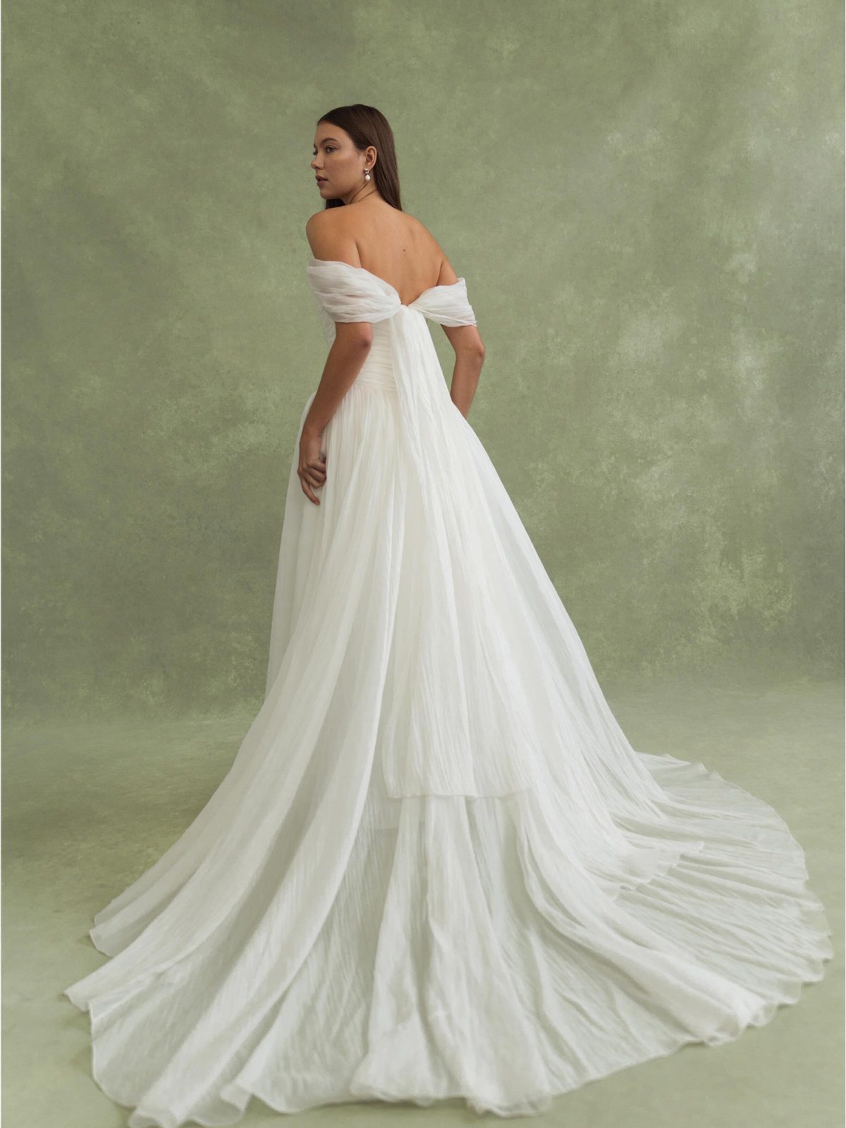 Woman wearing a white off-the-shoulder chiffon wedding dress with a long flowing train
