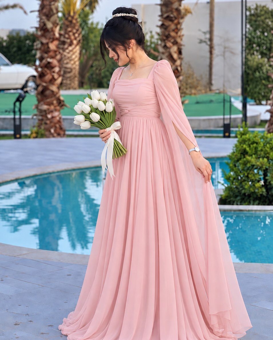 Woman in a flowing pink chiffon wedding dress holding white tulips by a pool