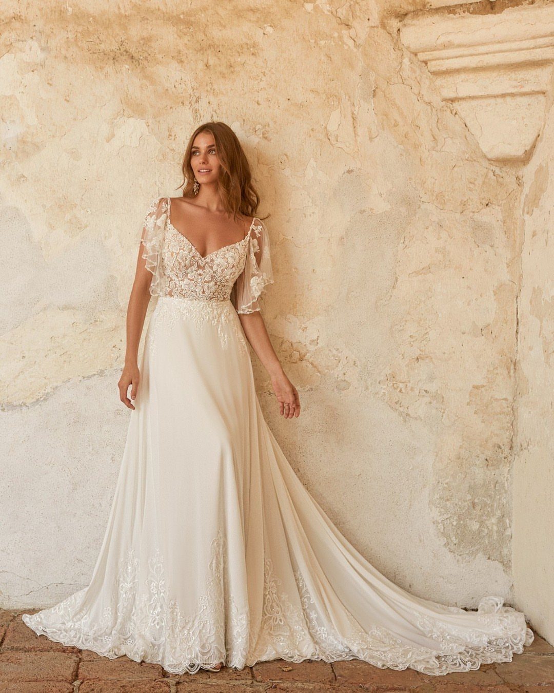 Woman in an ivory chiffon wedding dress with lace bodice against stone wall