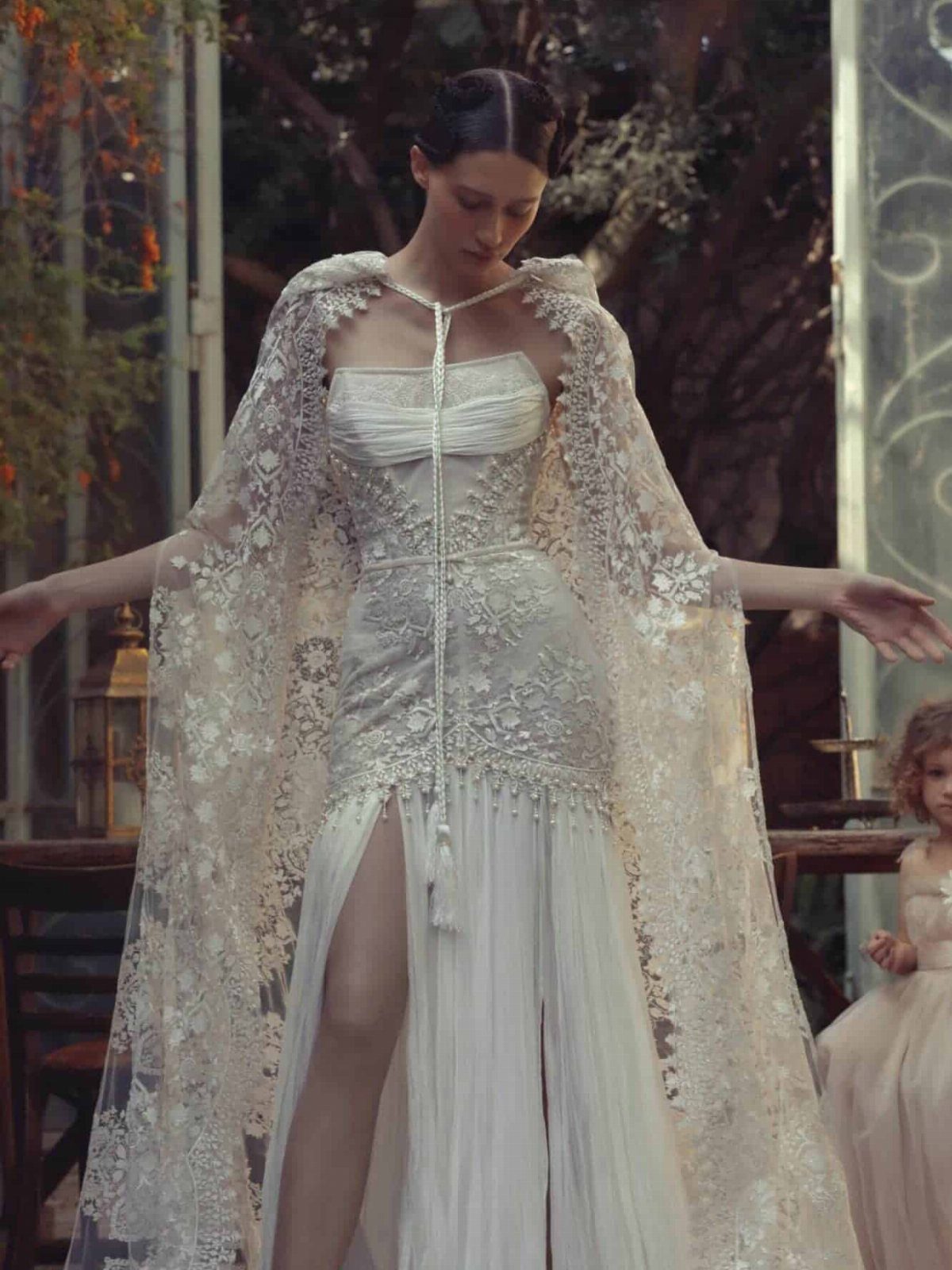 Woman in a white lace couture wedding dress with a matching long cape.