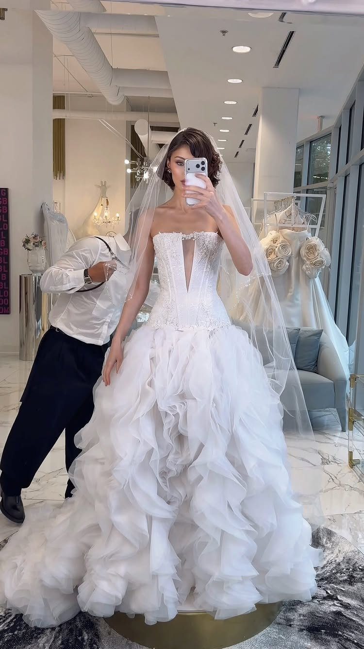 Woman in a ruffled white couture wedding dress being fitted by a tailor.