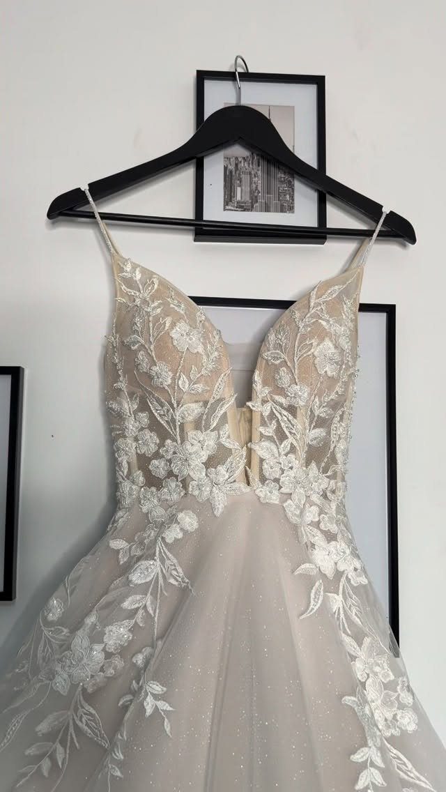 Champagne wedding dress with white floral lace appliqués hanging on a black hanger.