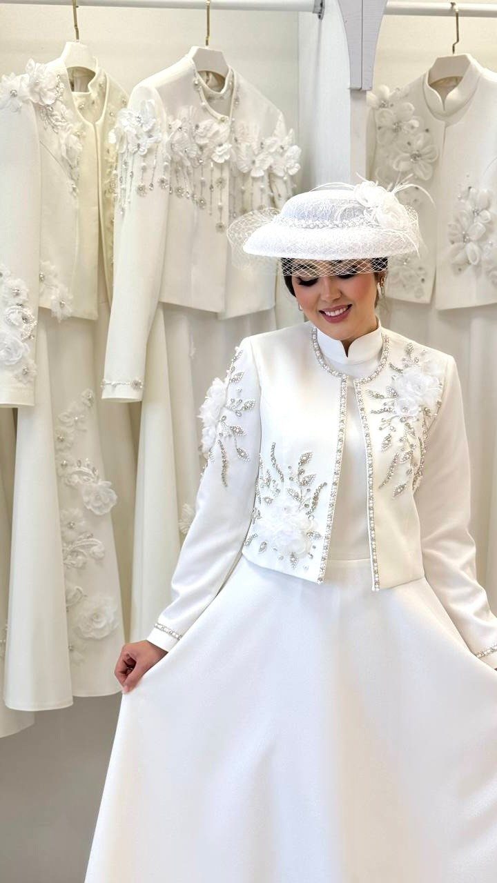 Woman in a white bridal gown wearing a cropped embroidered bridal jacket and hat.
