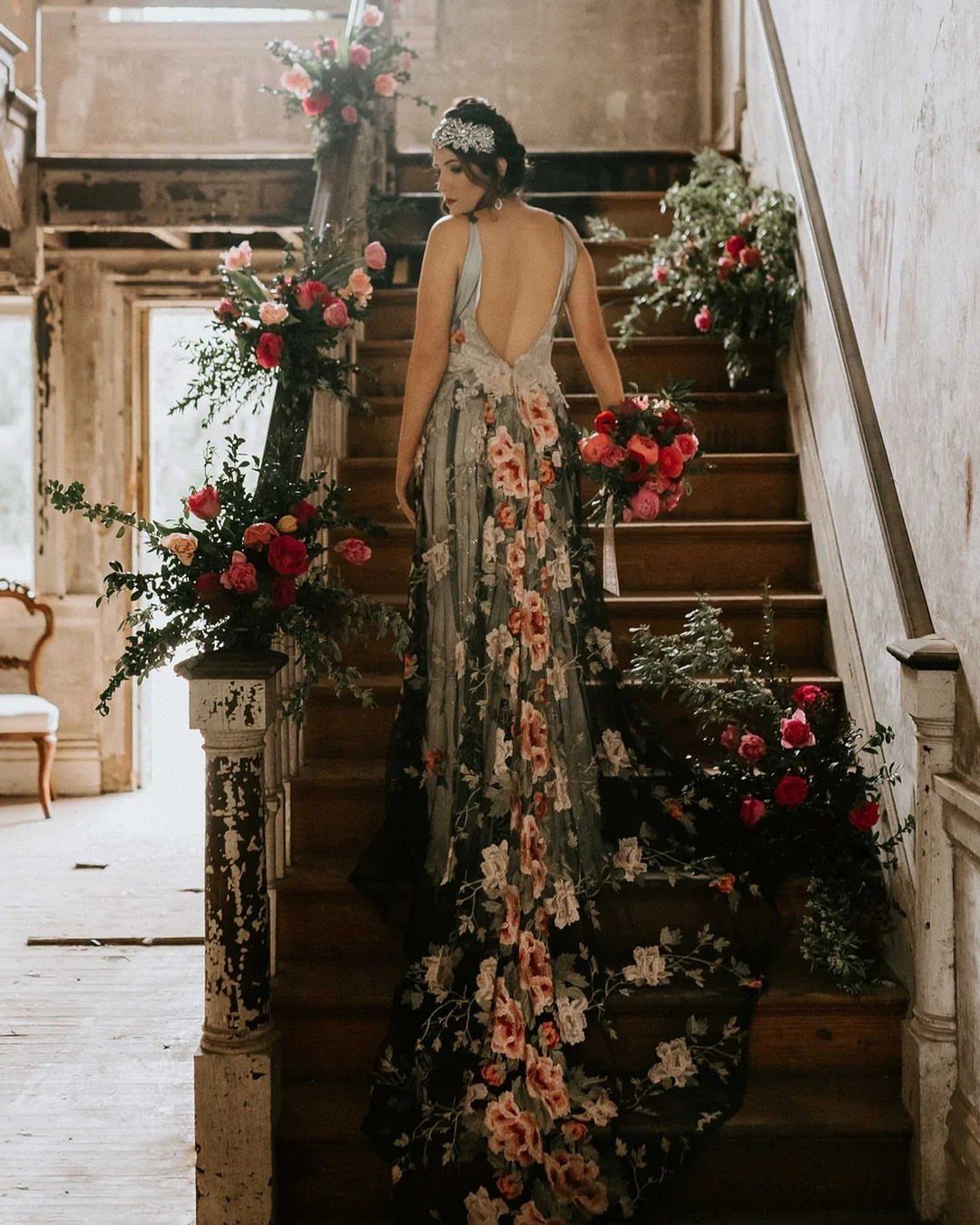 Woman in a dark floral print wedding dress standing on rustic wooden stairs.