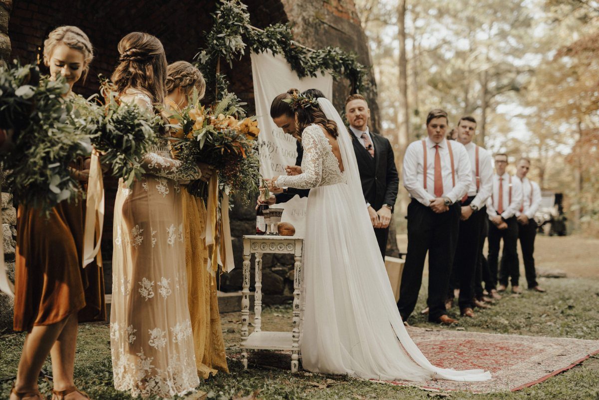 Bride in long-sleeved lace wedding dress with a dramatic train at outdoor ceremony