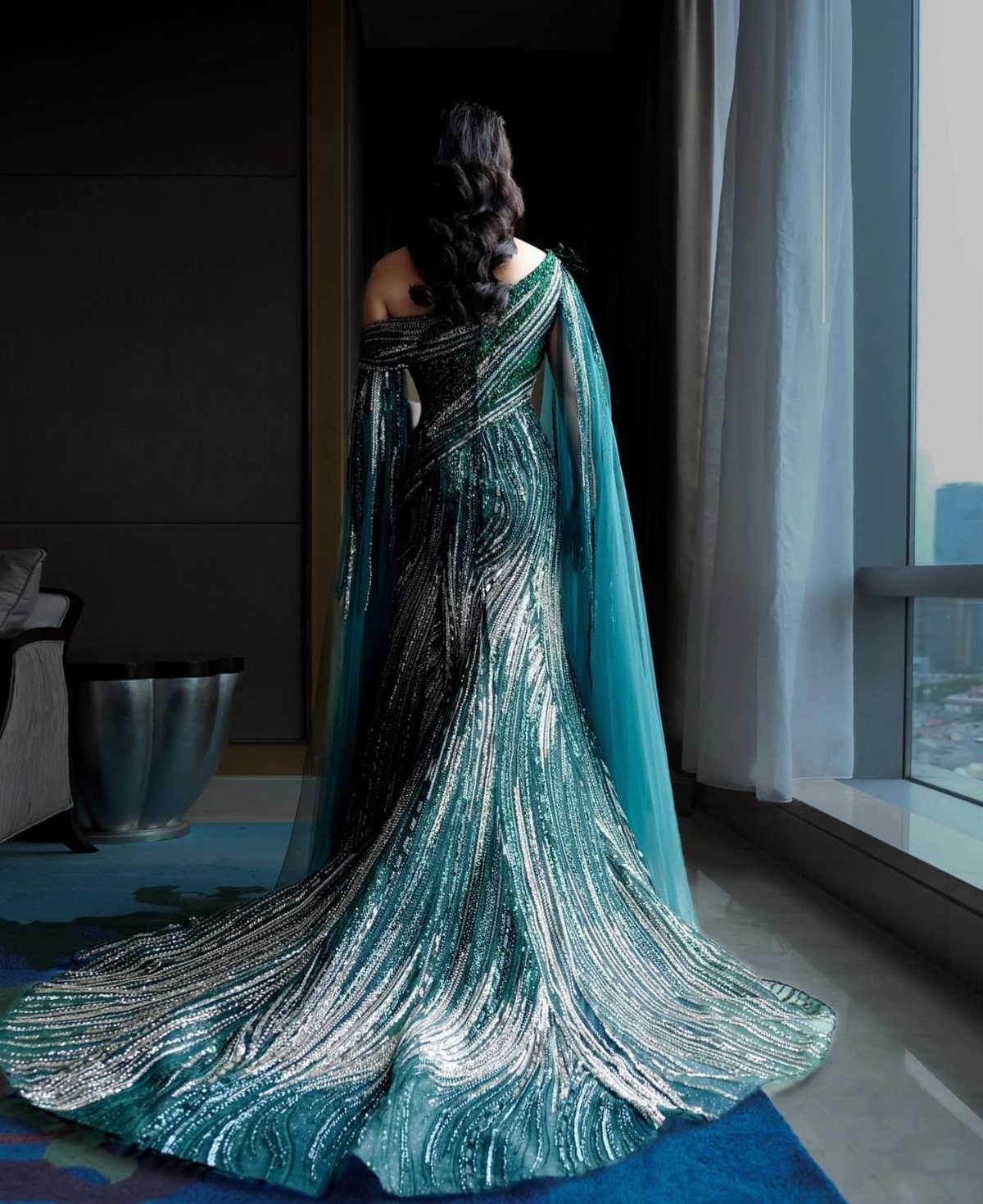 Woman in a shimmering teal and silver gown with a long dramatic train.