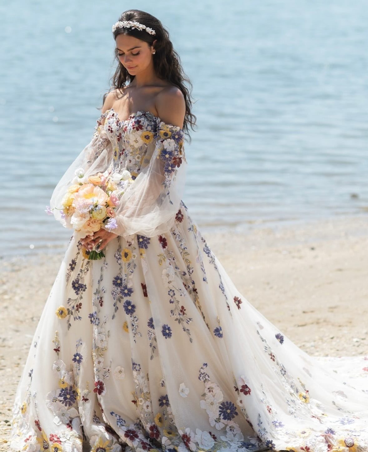 Woman in a floral embroidered bohemian wedding dress standing on a sandy beach.