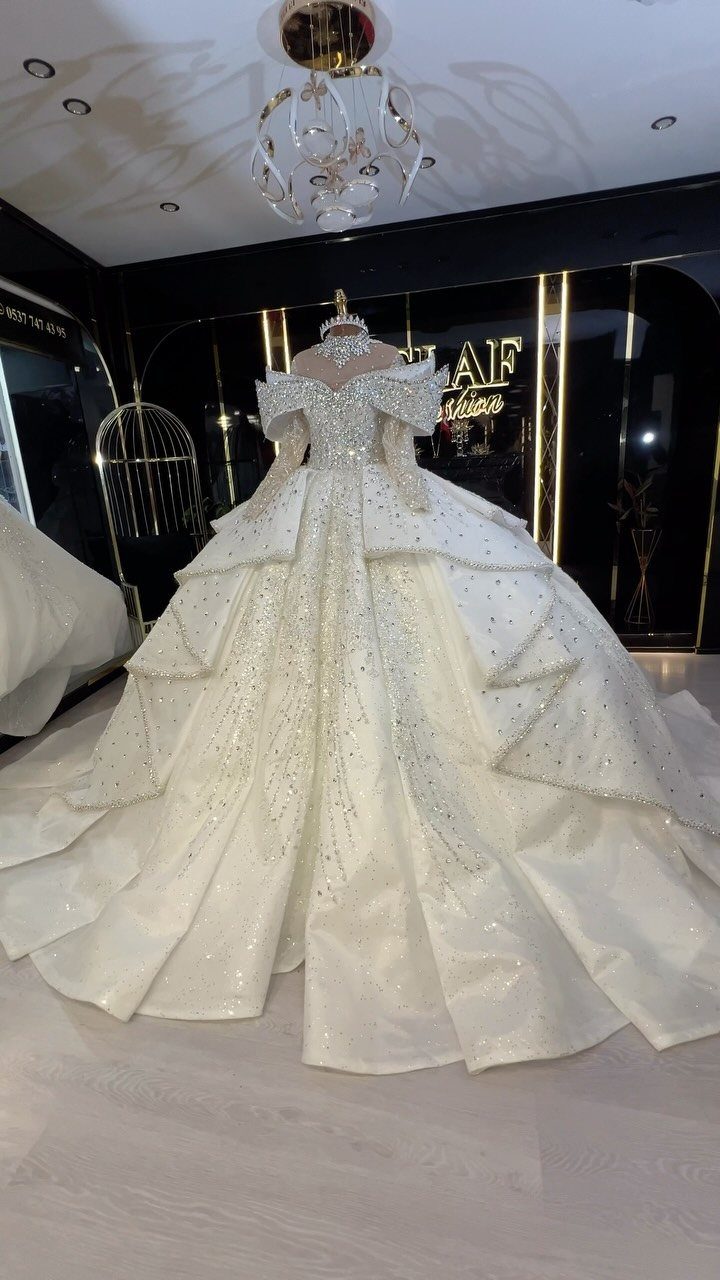 Voluminous white wedding dress with beaded details and layered skirt on a mannequin.