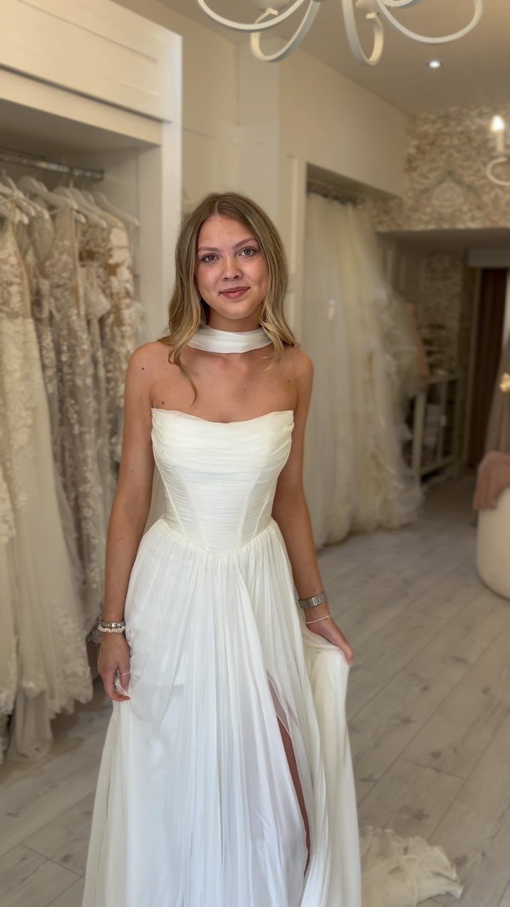 Woman in a white strapless A-line wedding dress standing in a bridal boutique.