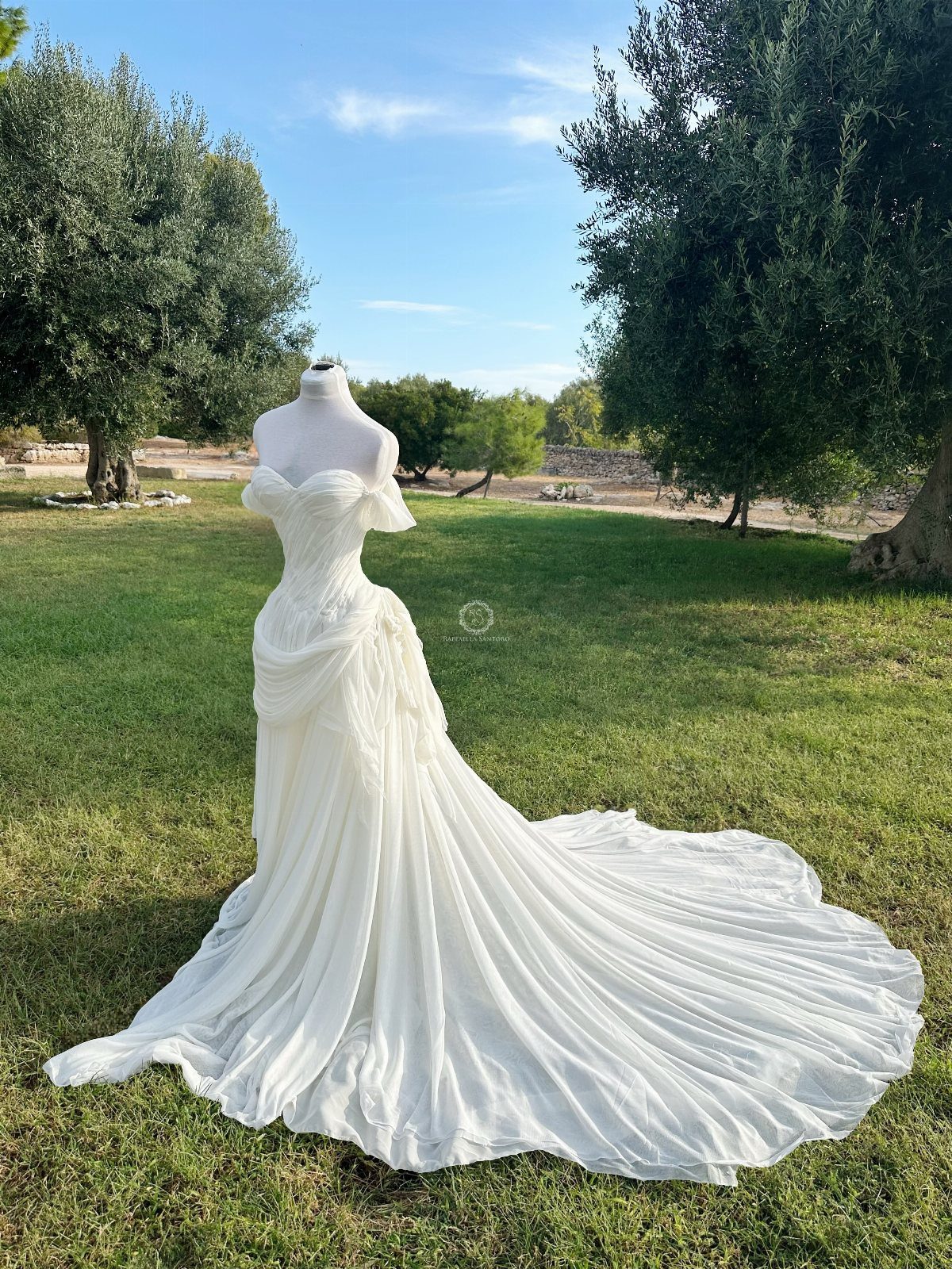 White flowy wedding dress on a mannequin in a sunny green field