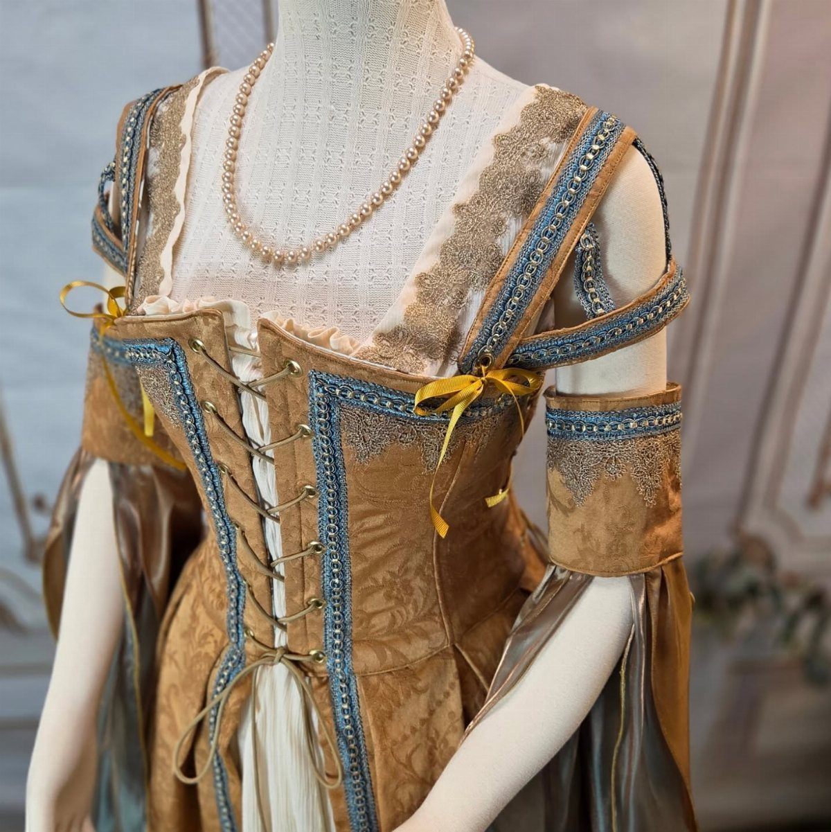 Gold and blue medieval gown on a mannequin featuring a laced corset closure.