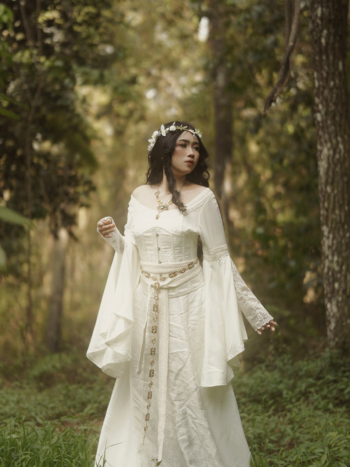Woman in a white medieval wedding dress and floral crown in a forest