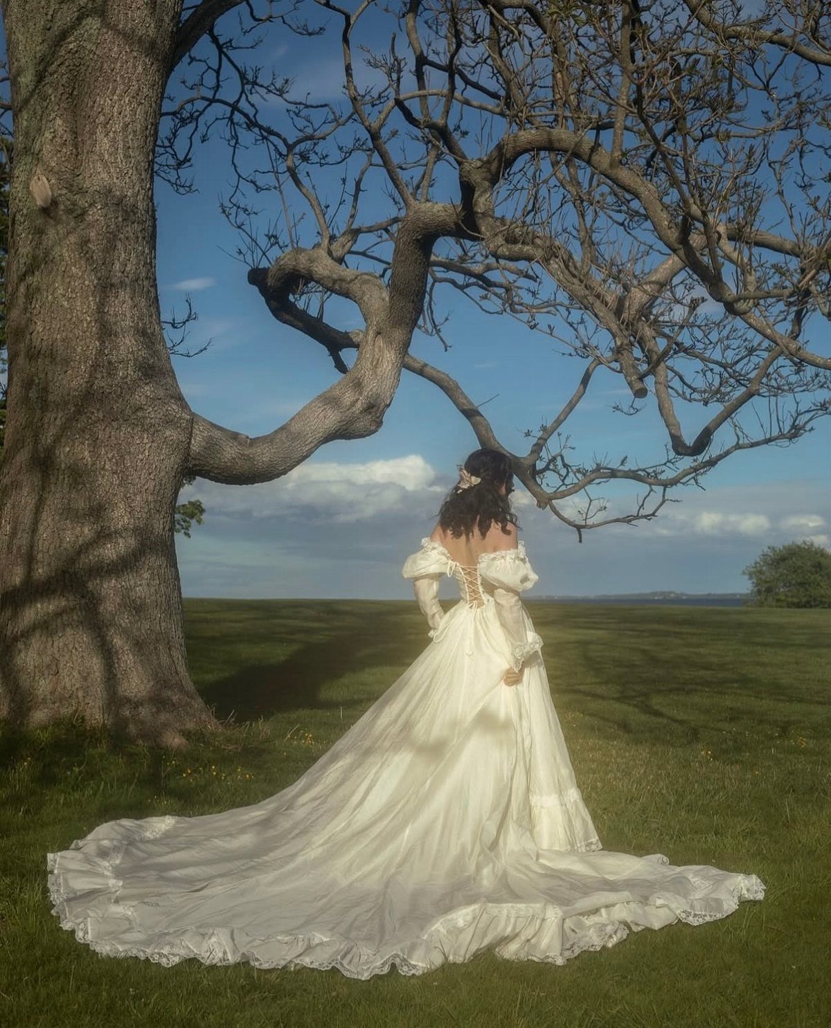 Woman in a white medieval wedding gown standing under a large leafless tree