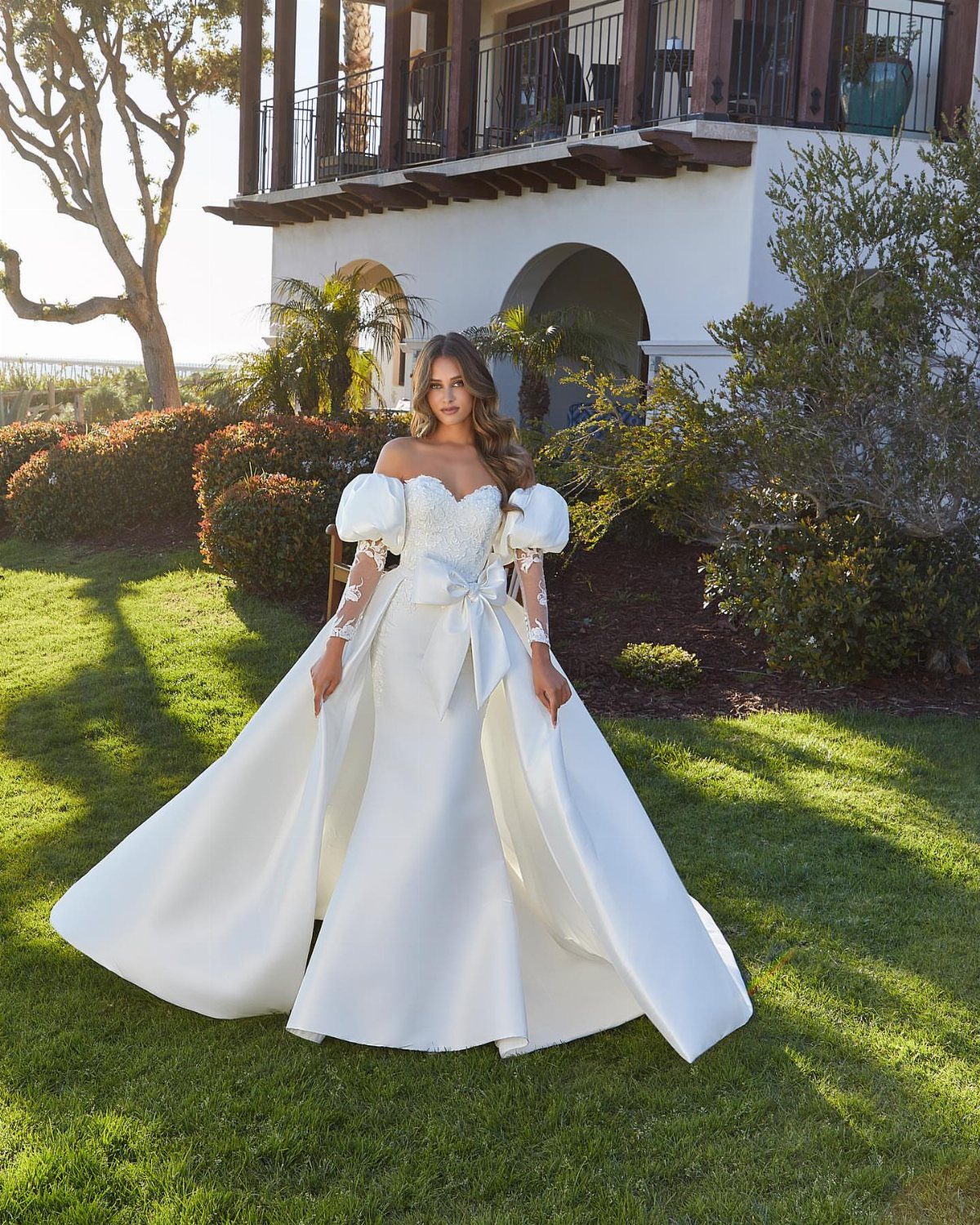 Woman in a white satin wedding dress with puffed sleeves standing on green grass.
