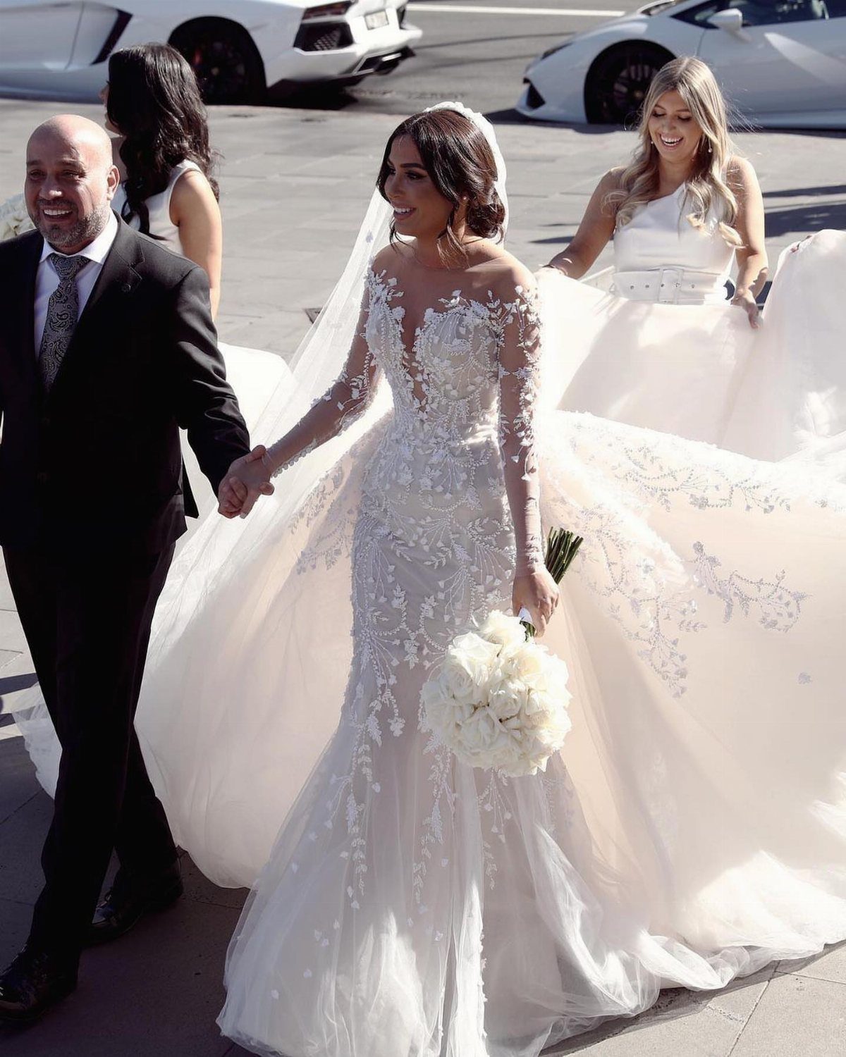 Bride in a lace mermaid wedding dress walking with her groom outdoors.