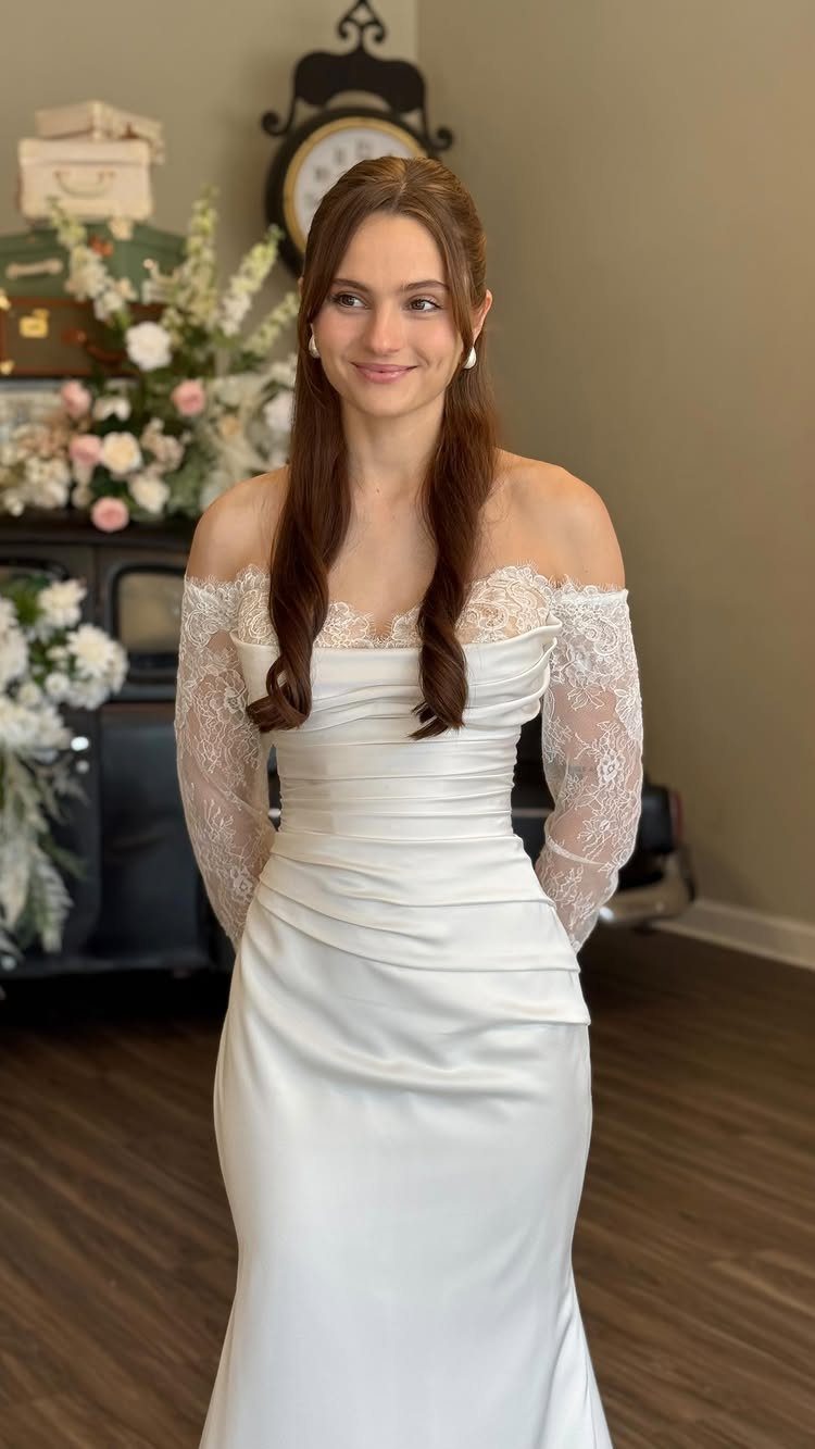 Woman wearing a white off-the-shoulder sleek sheath wedding dress with lace sleeves.