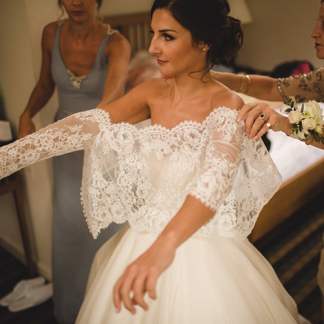 Bride wearing a white lace shawl over her wedding dress while being assisted.