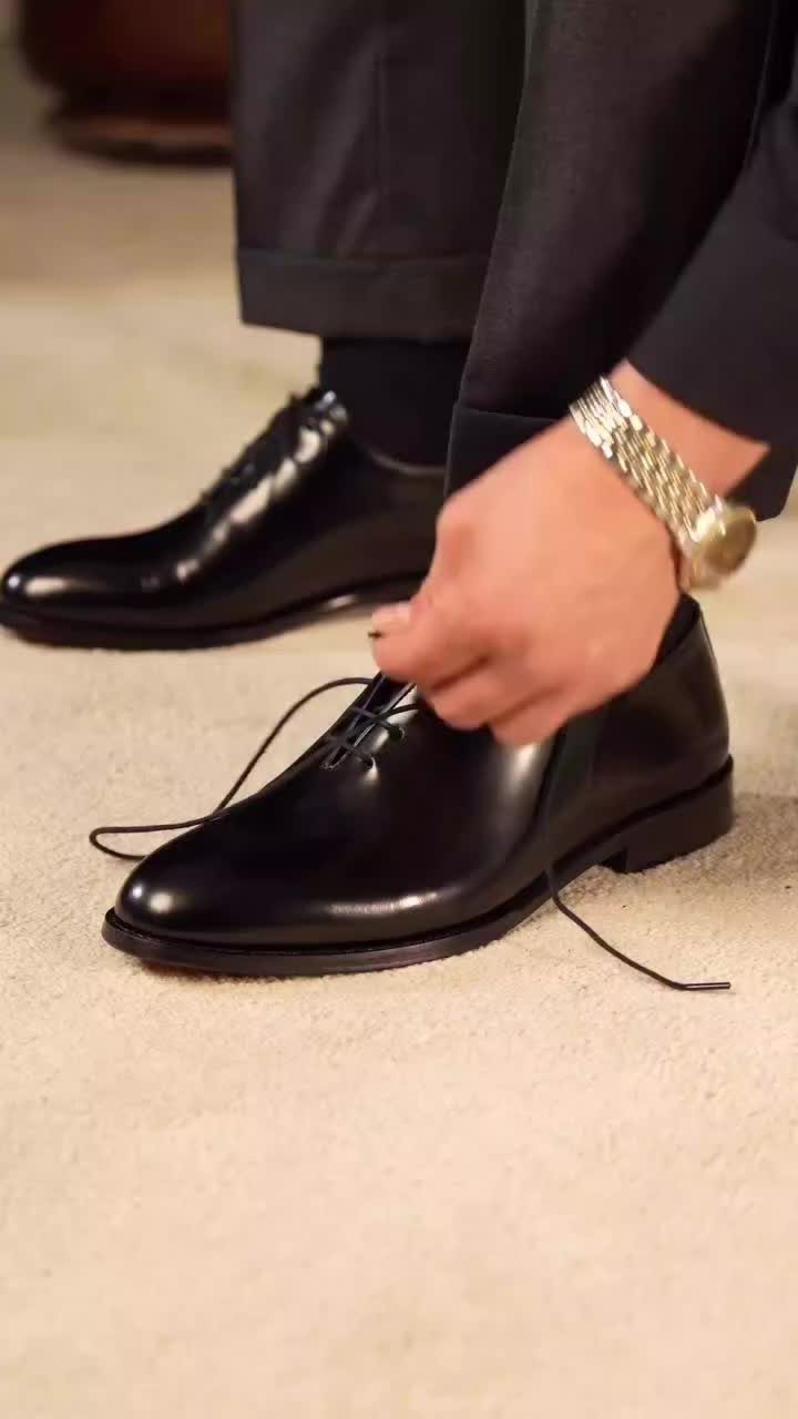 Black leather oxford dress shoes being tied by a person in black trousers.