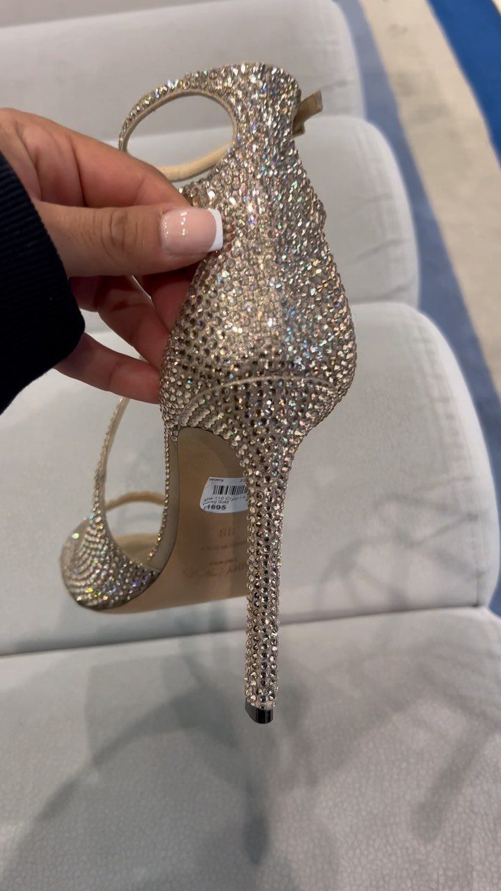 Sparkling silver rhinestone high-heeled bridal shoe held by a hand.