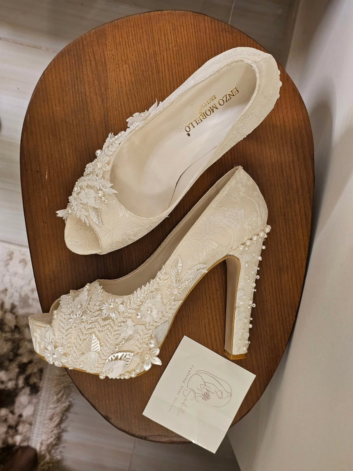 Cream bridal high heels with floral lace and pearl embellishments on wooden table