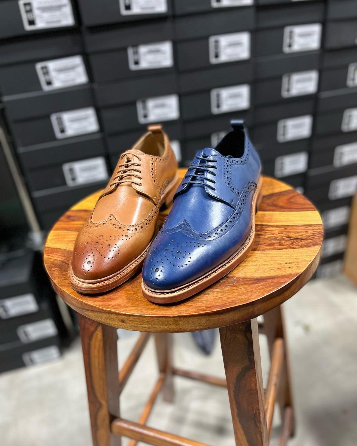 Tan and blue leather wingtip brogue shoes on a round wooden stool.