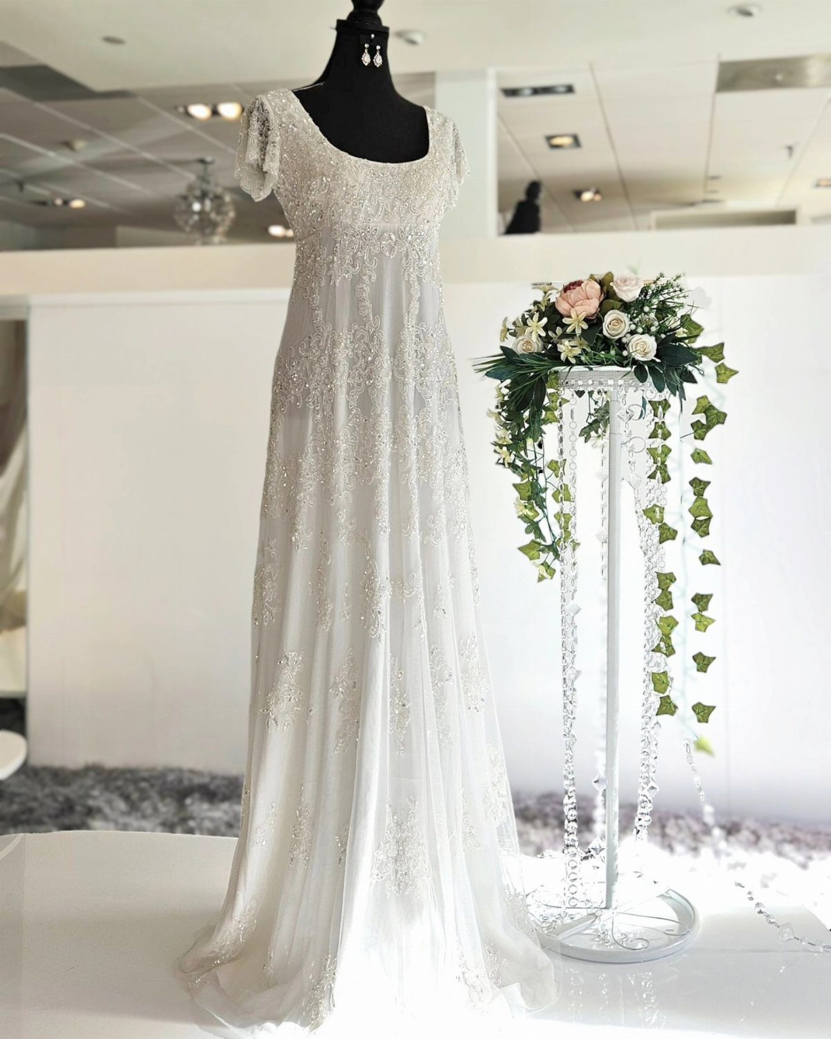 White beaded wedding dress with empire waist on a mannequin next to flowers