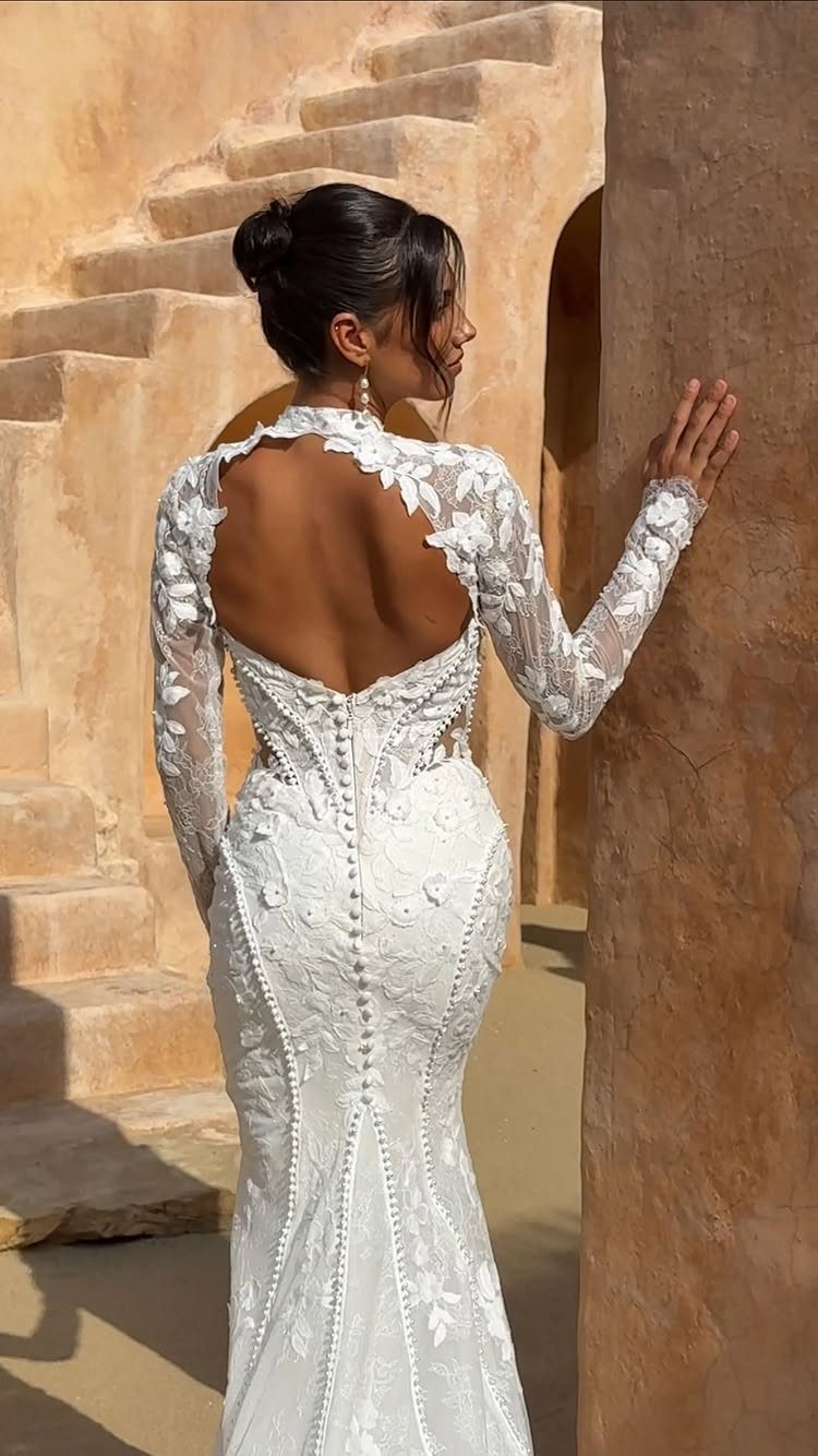 Woman in a white lace fit-and-flare wedding dress standing by a stone wall.