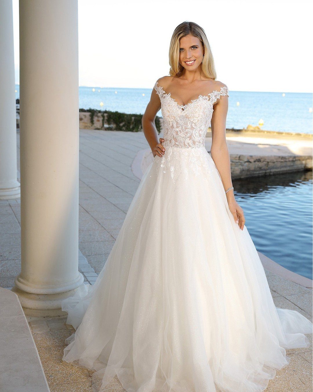 Woman in a white A-line wedding dress standing by a column near the ocean