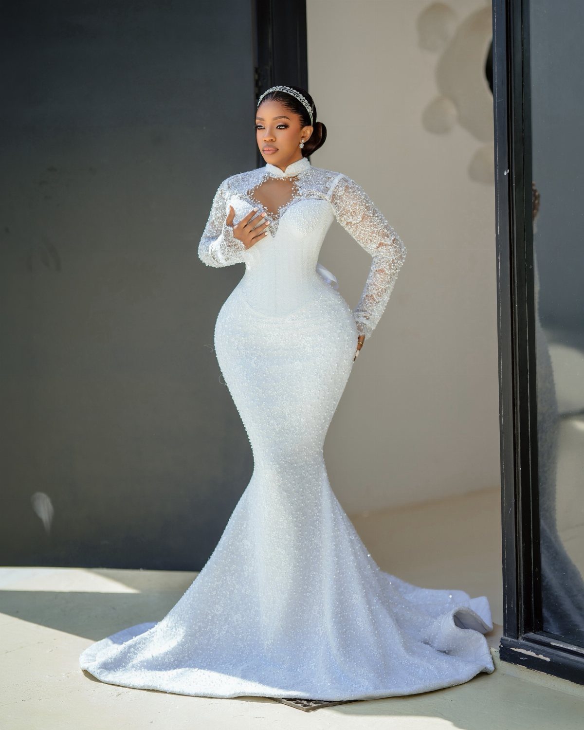 Woman in a white sparkling mermaid wedding dress with lace sleeves posing outdoors.