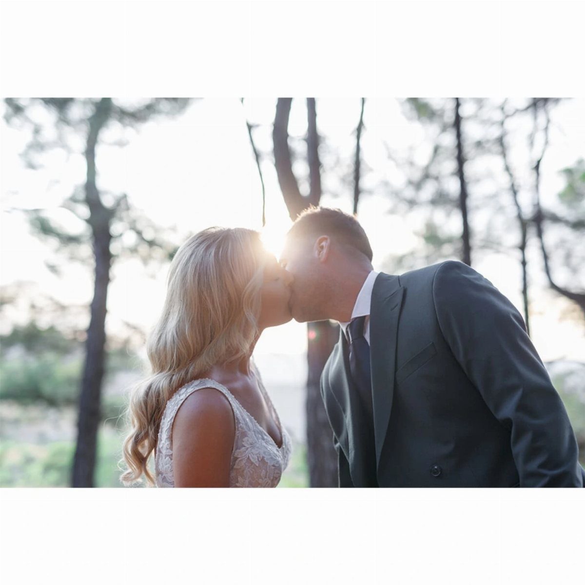 Bride in lace dress and groom in grey suit kissing in a forest